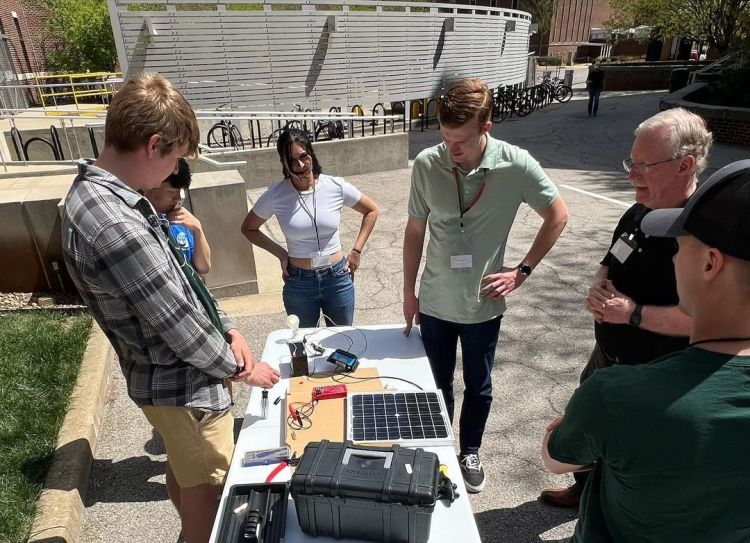 A group of people standing around a mini solar panel demonstration